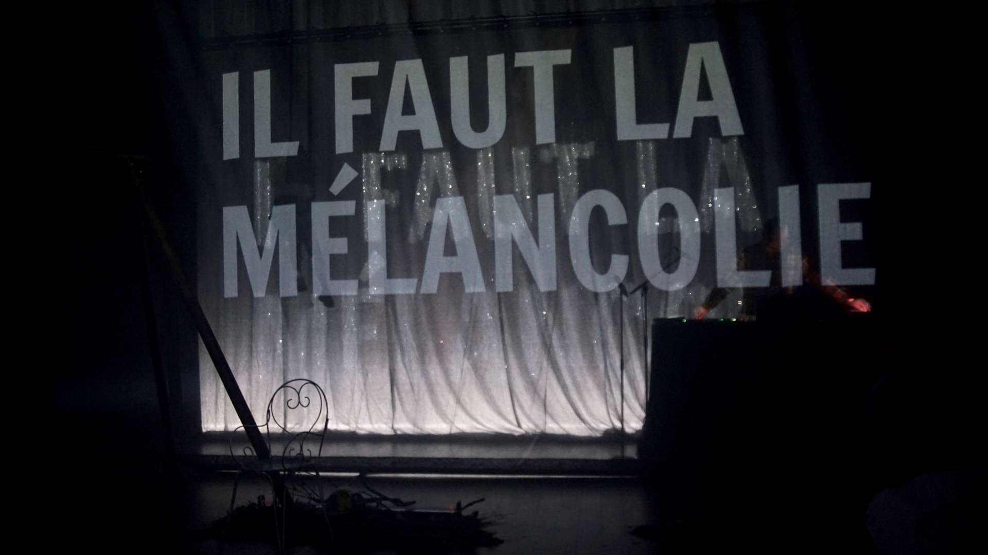 Sur une scène de théâtre le texte Il faut la mélancolie projeté