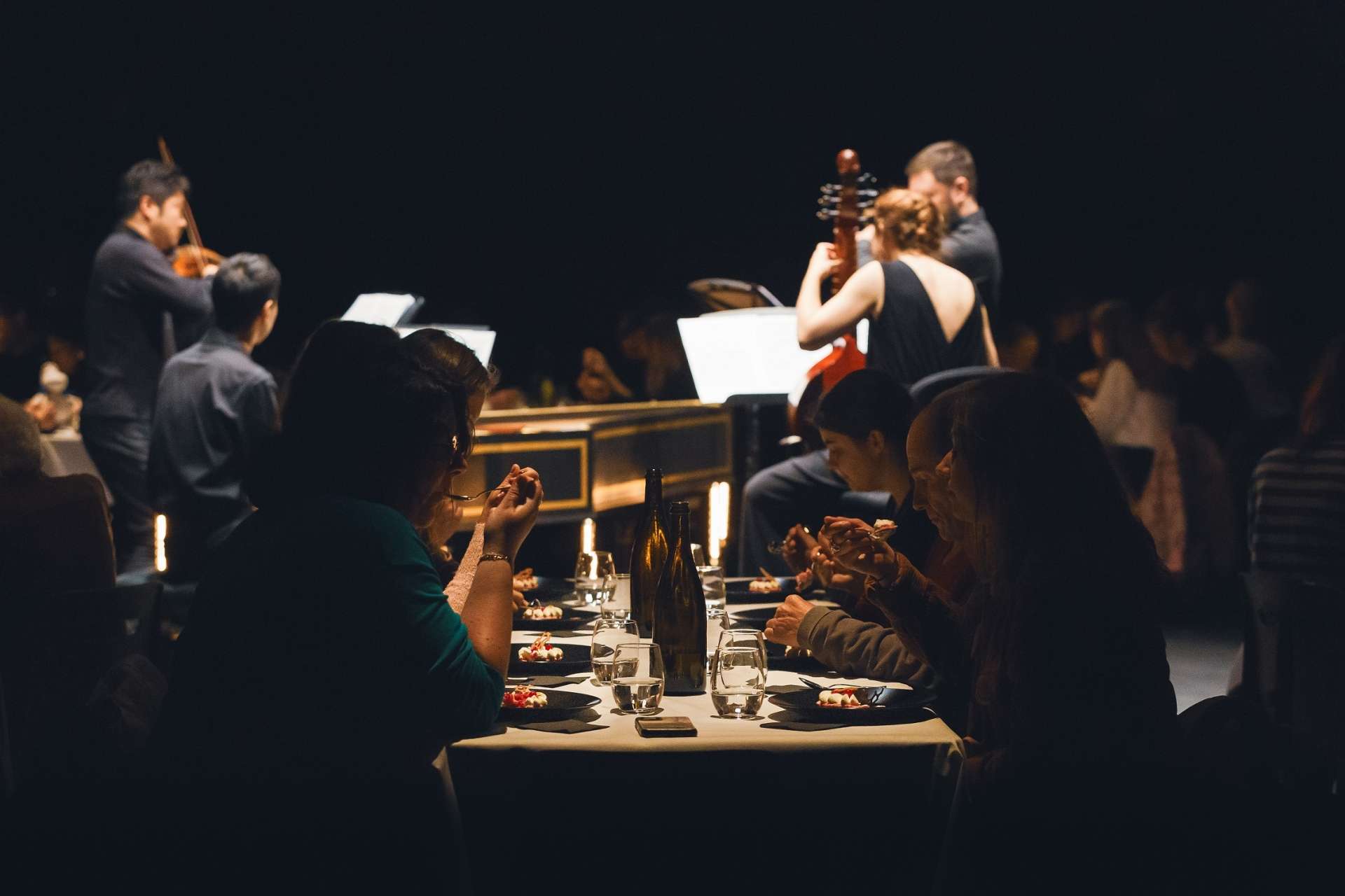 Au premier plan dans l'obscurité, des convives qui dégustent un dessert et au milieu, les quatre musiciens qui jouent pour éveiller les sens. 