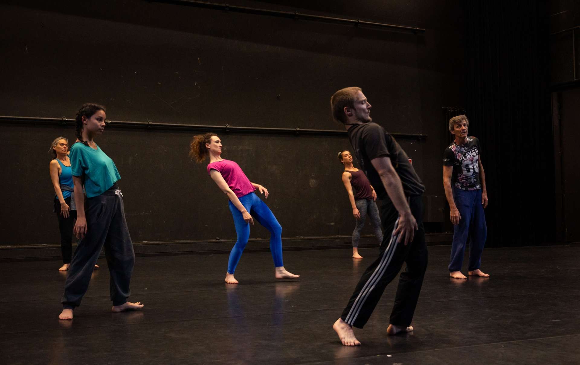 Photo de l'atelier de danse acrobatique, Clotaire en premier plan montre un pas de danse, debout le haut du corps en arrière. Les participant·es suivent le mouvement.