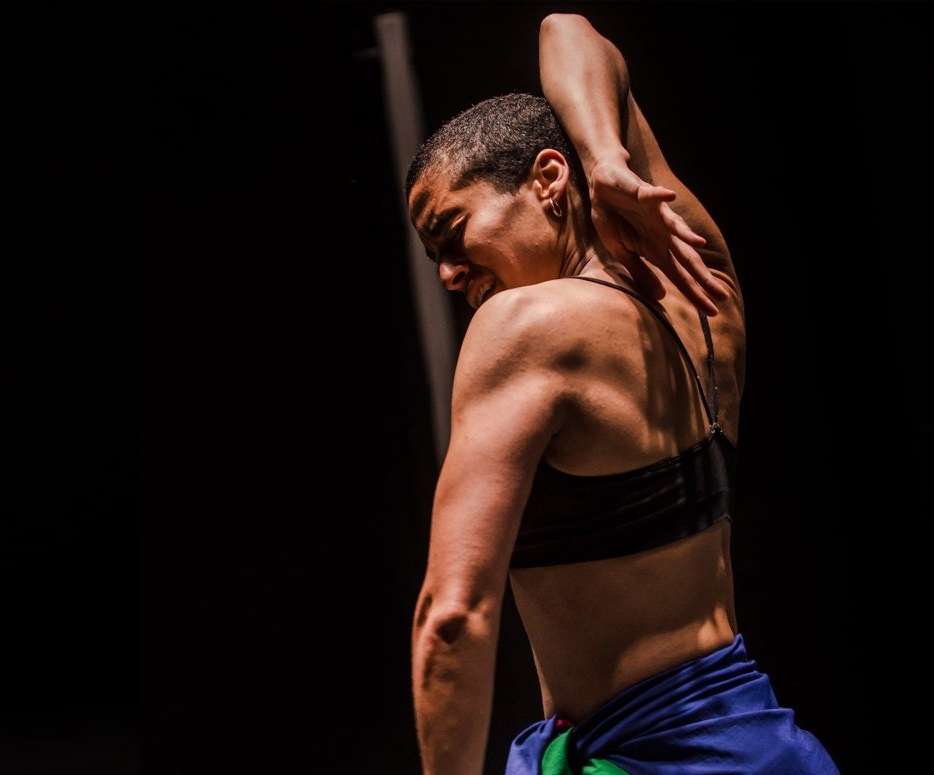Photo de Nach, en train de danser. Vue de dos, les bras en arrière et le visage de profile, un expression de douleur sur le visage, ressentant les émotions de la danse. 