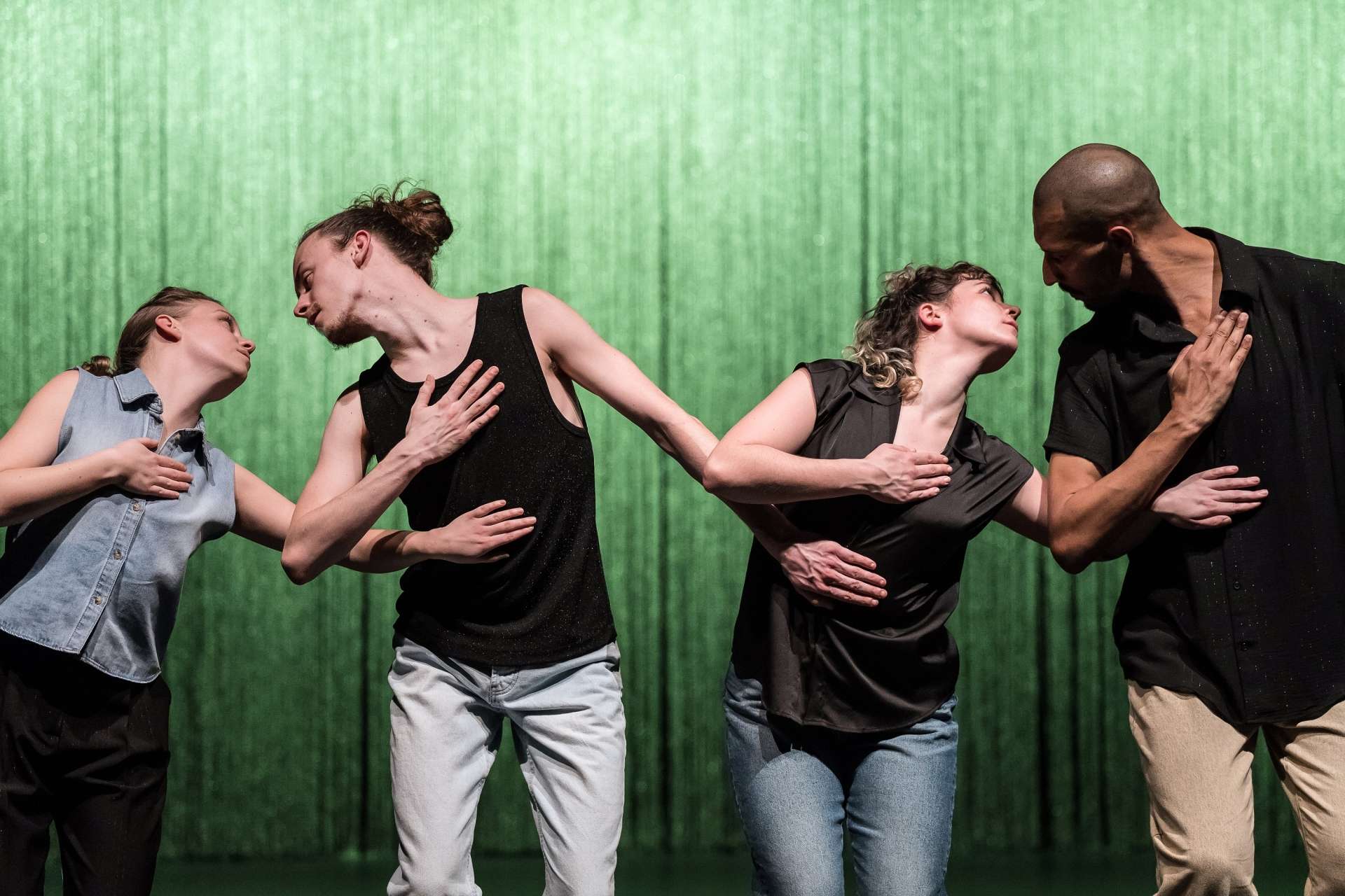 Photo du spectacle "d'amour", deux danseurs et deux danseuses disposés en deux paires, chacune en interaction, ils se regardent dans les yeux, leurs mains sur le cœur. L'utilisation d'un arrière-plan uni de couleur vert pâle met les danseurs en valeur. 