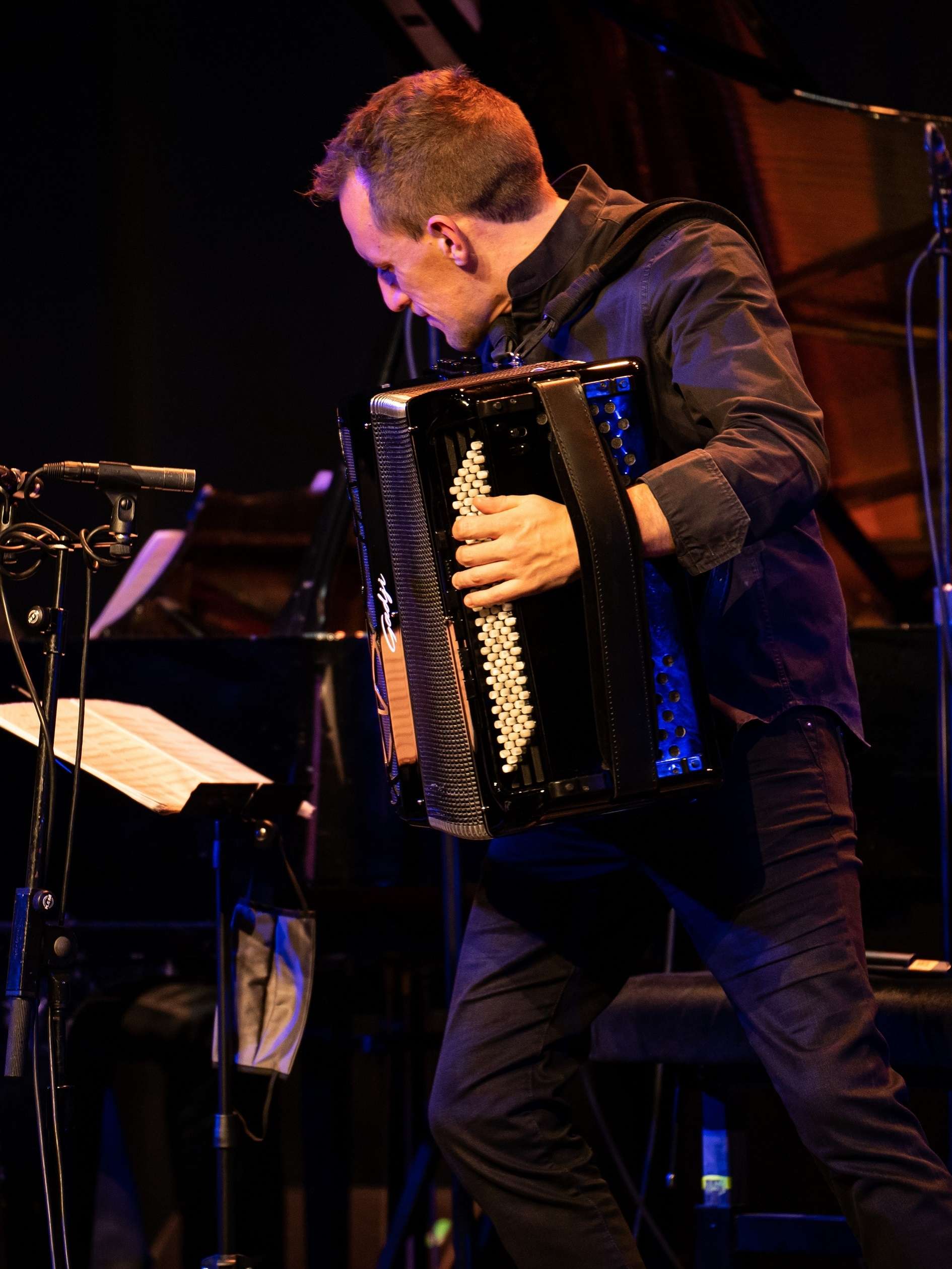 Photo de Félicien Brut, accordéon en main, sur scène en train de jouer. Des pupitres avec les partitions sont devant lui.
