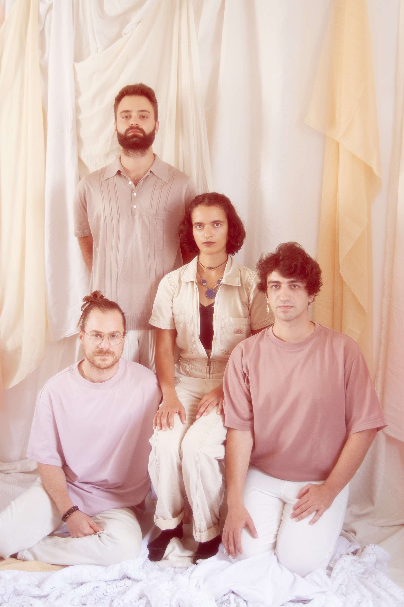 Portrait du groupe MarsAvril : les 4 artistes sont assis dans un décor aux ton pastels : crème et rose. Ils sont habillés de ces mêmes couleurs. 