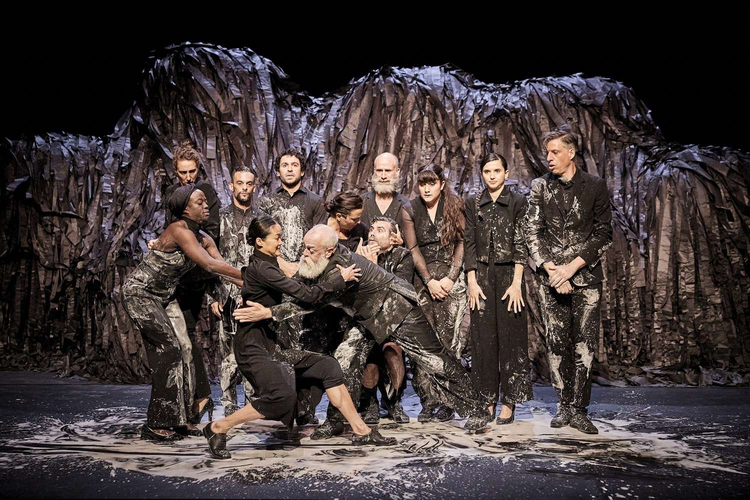 Photo des artistes du spectacle "Qui som ?", rassemblés devant la structure en morceaux de tissu. Ils et elles regardent le public en face sauf quelques personnes en premier plan qui s'enlacent.