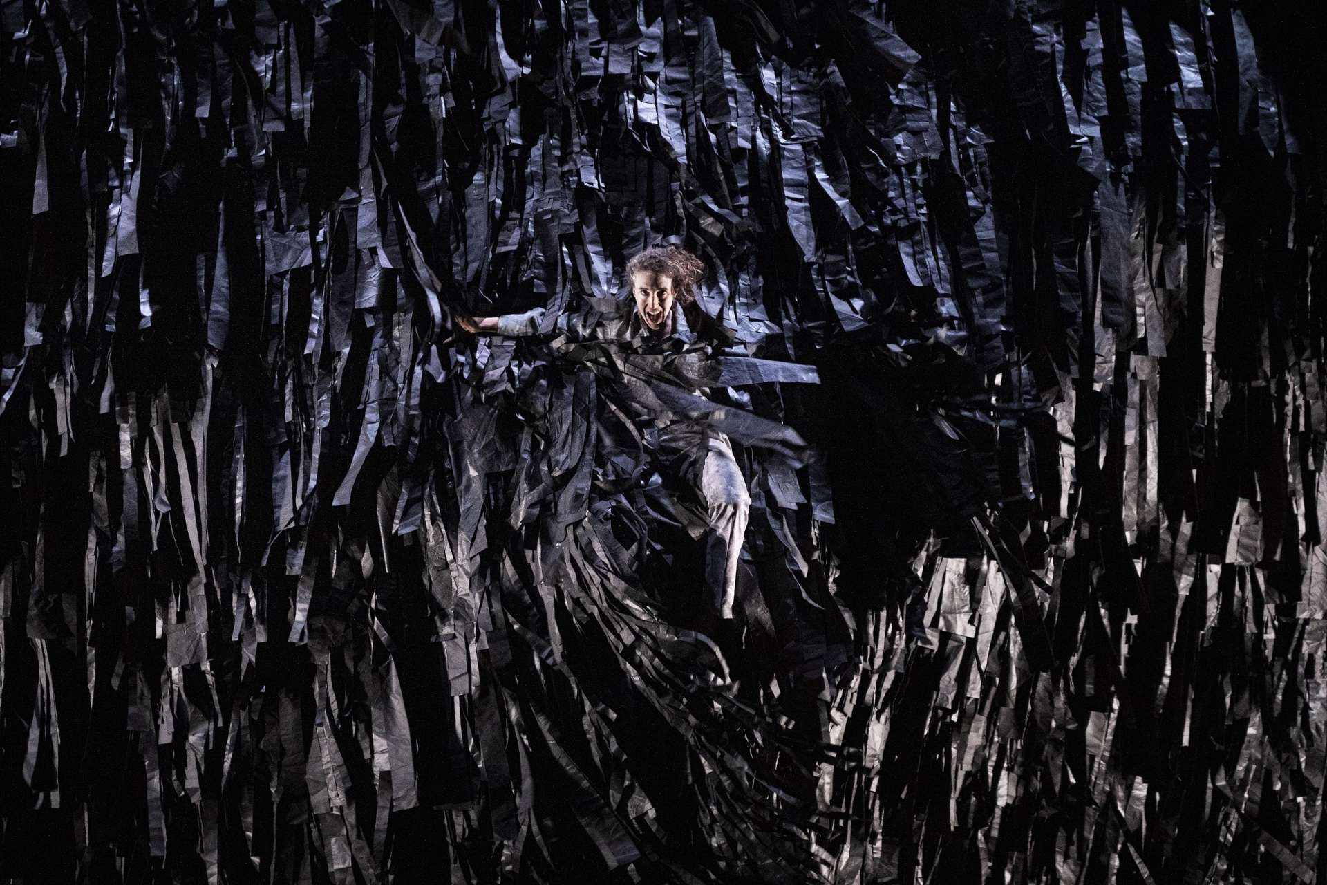 Photo d'une danseuse emprisonnée dans une structure faite de morceaux de tissu noir. Elle semble crier et tenter de se libérer. 