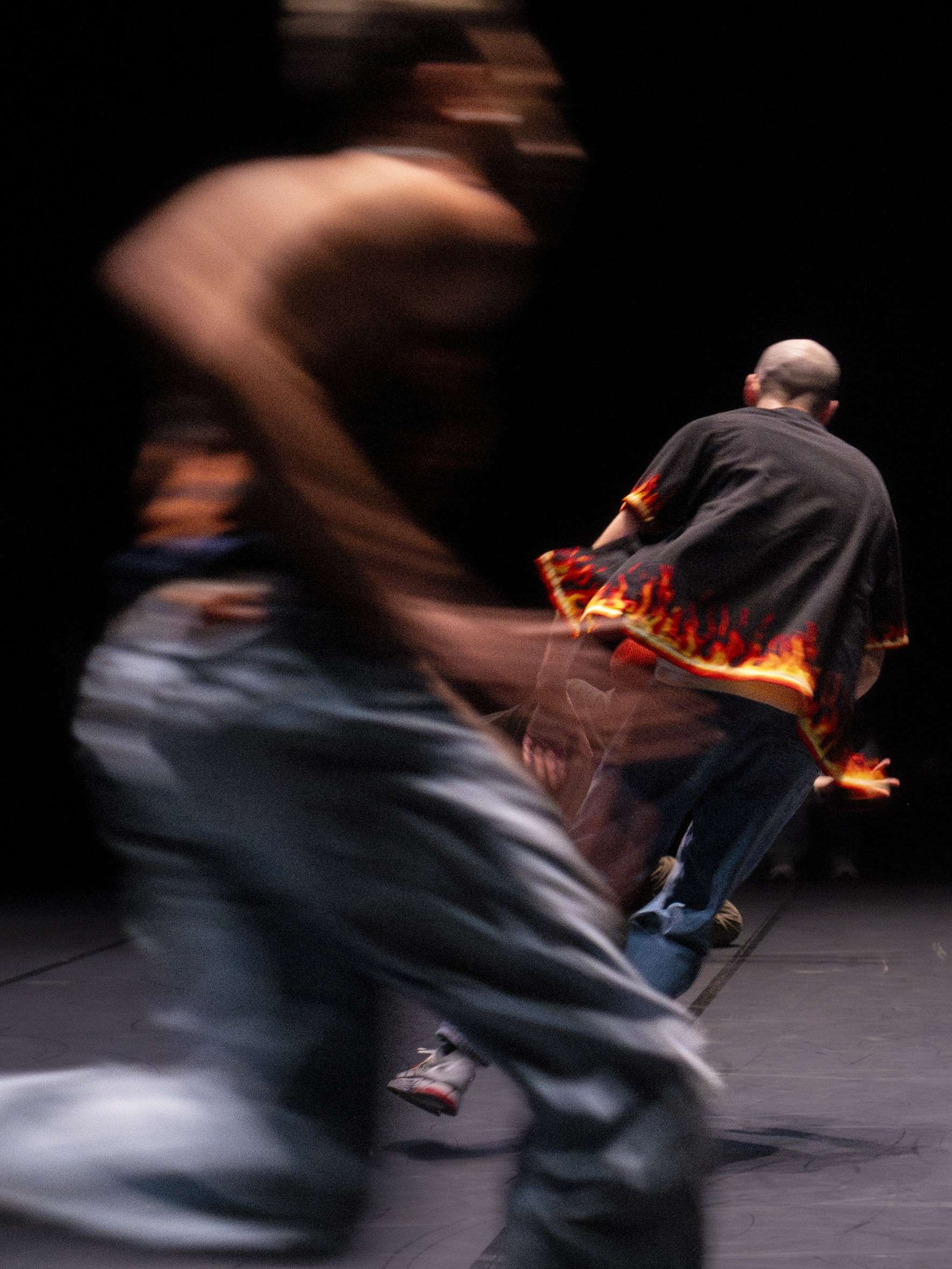 Photo focus sur deux personnes. Au premier plan, une jeune femme est en pleine course, son mouvement est flou. Derrière elle, un homme court également, habillé d'un gilet avec des flammes. 