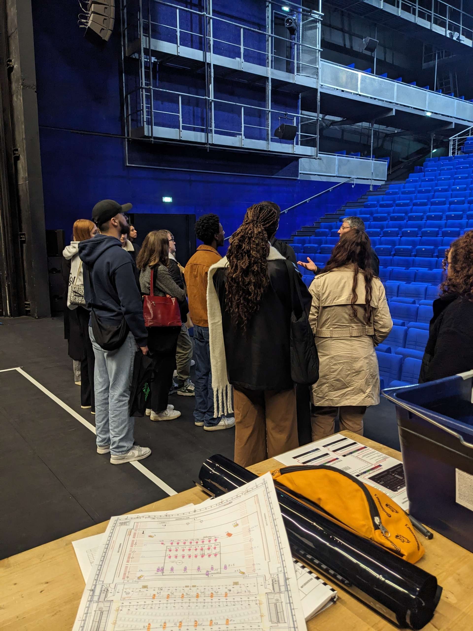 Photo d'une visite du Théâtre avec les élèves de l'école Pigier. Aperçu de la salle Barrault et de ses fauteuils bleus, ainsi qu'une table avec des documents (un plan de la salle par exemple)