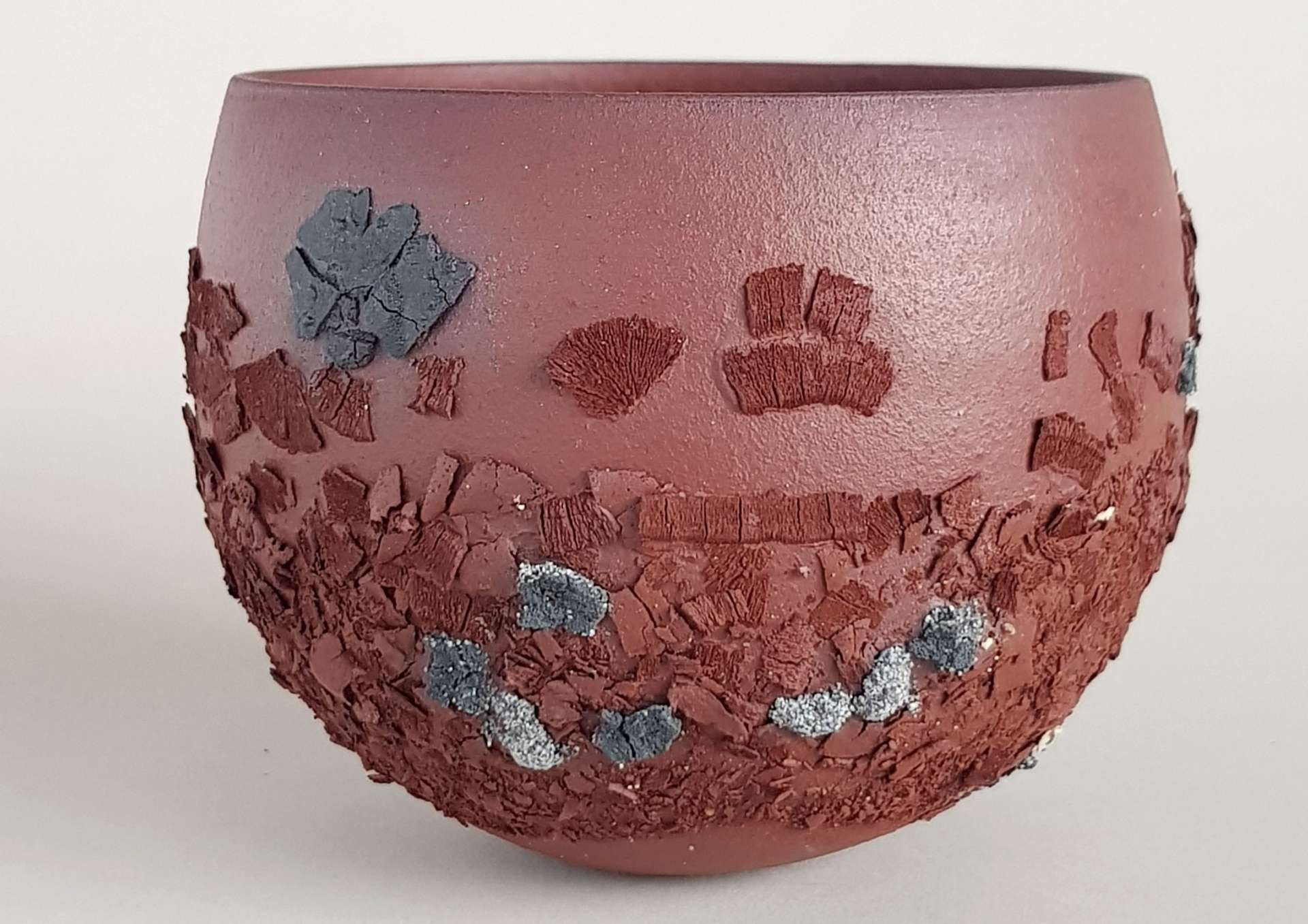 Sur fond blanc, photo d'une œuvre d'art en céramique qui ressemble à un bol marron décoré avec des éléments verts et blancs. 