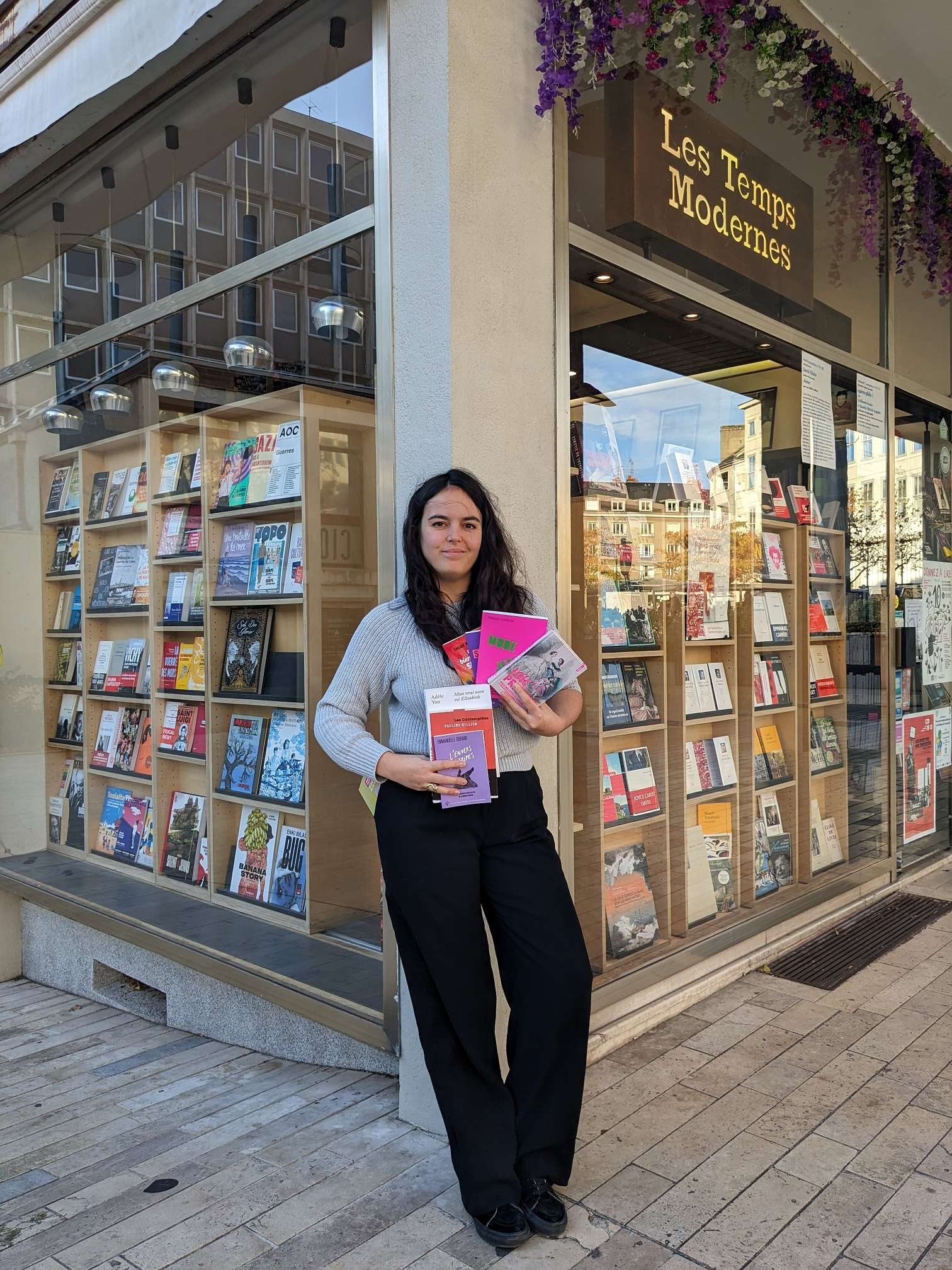 Photo de la libraire Deborah Vedel posant devant la devanture de la Librairie Les Temps Modernes. 