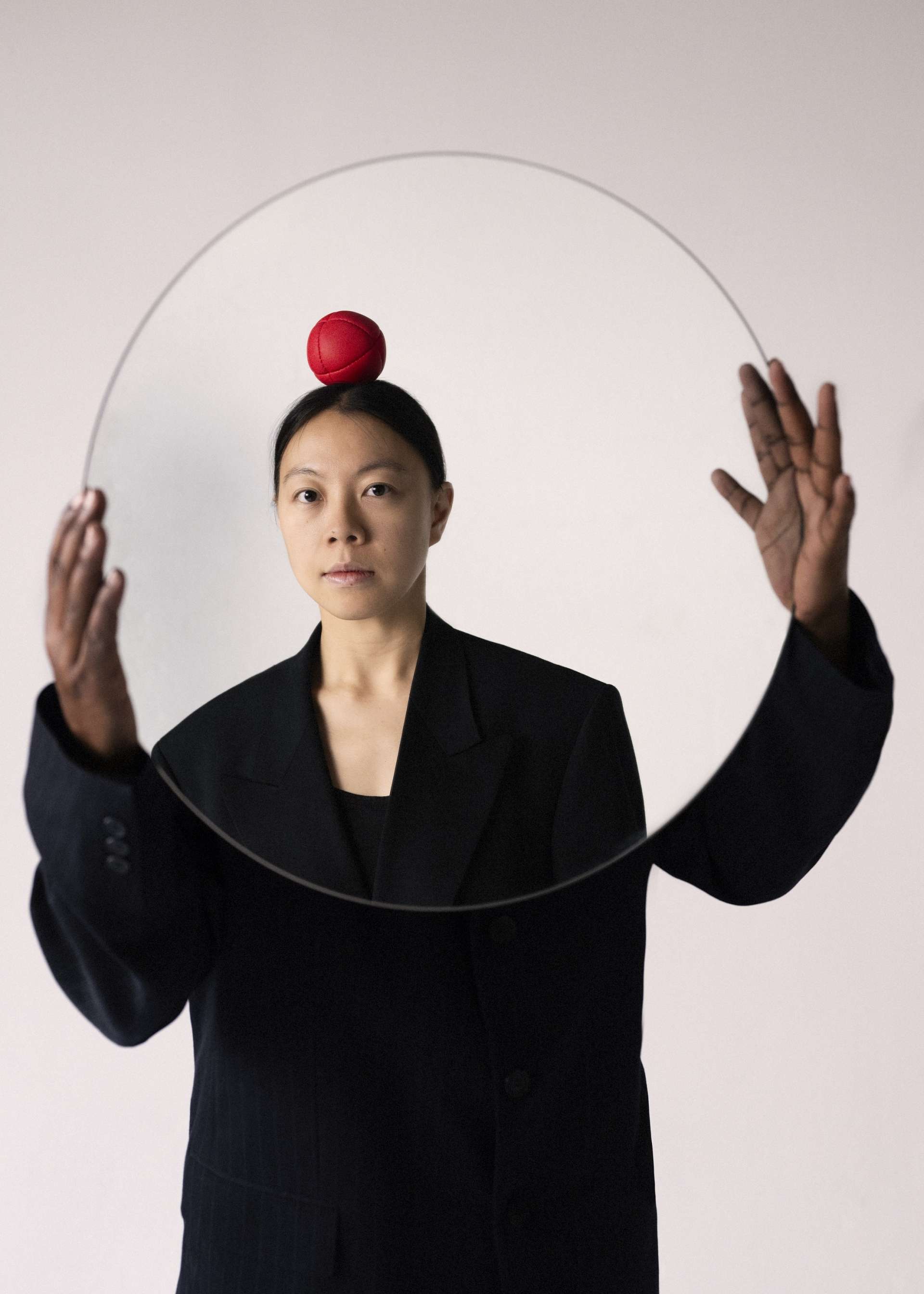 Personne en costume noir. Sa tête est remplacée par un miroir dans lequel on aperçoit une femme avec une balle rouge sur sa tête. Il y a un effet visuel entre les deux corps qui ne pourraient faire qu'un.