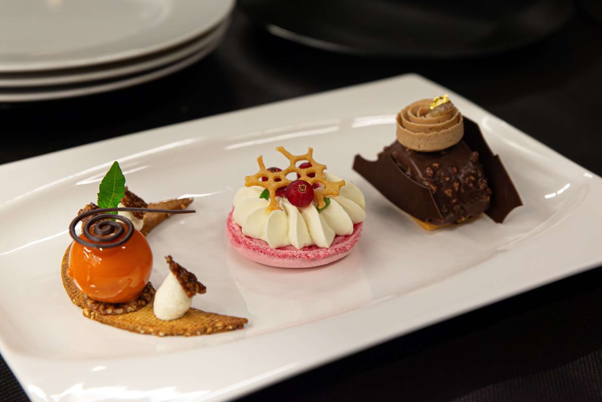 Gros plan sur les trois pâtisseries présentées dans une même assiette et dans l'ordre suivant : La nuit orientale, L’écrin sucré et le Mont cassis. 