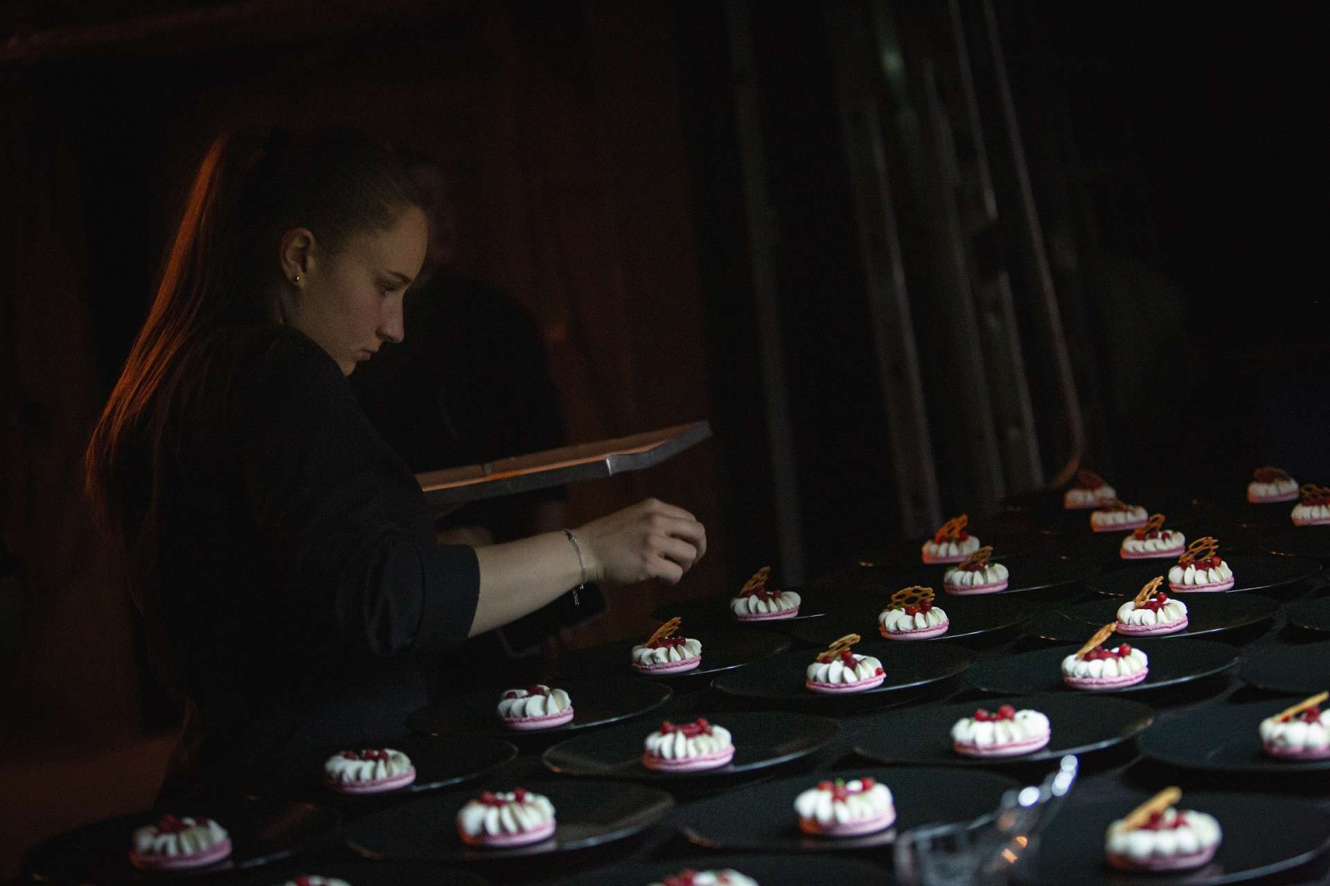 Une apprentie pâtissière est en train de donner la touche final à son dessert L’écrin sucré. Il y a une multitude d'assiettes préparées. 