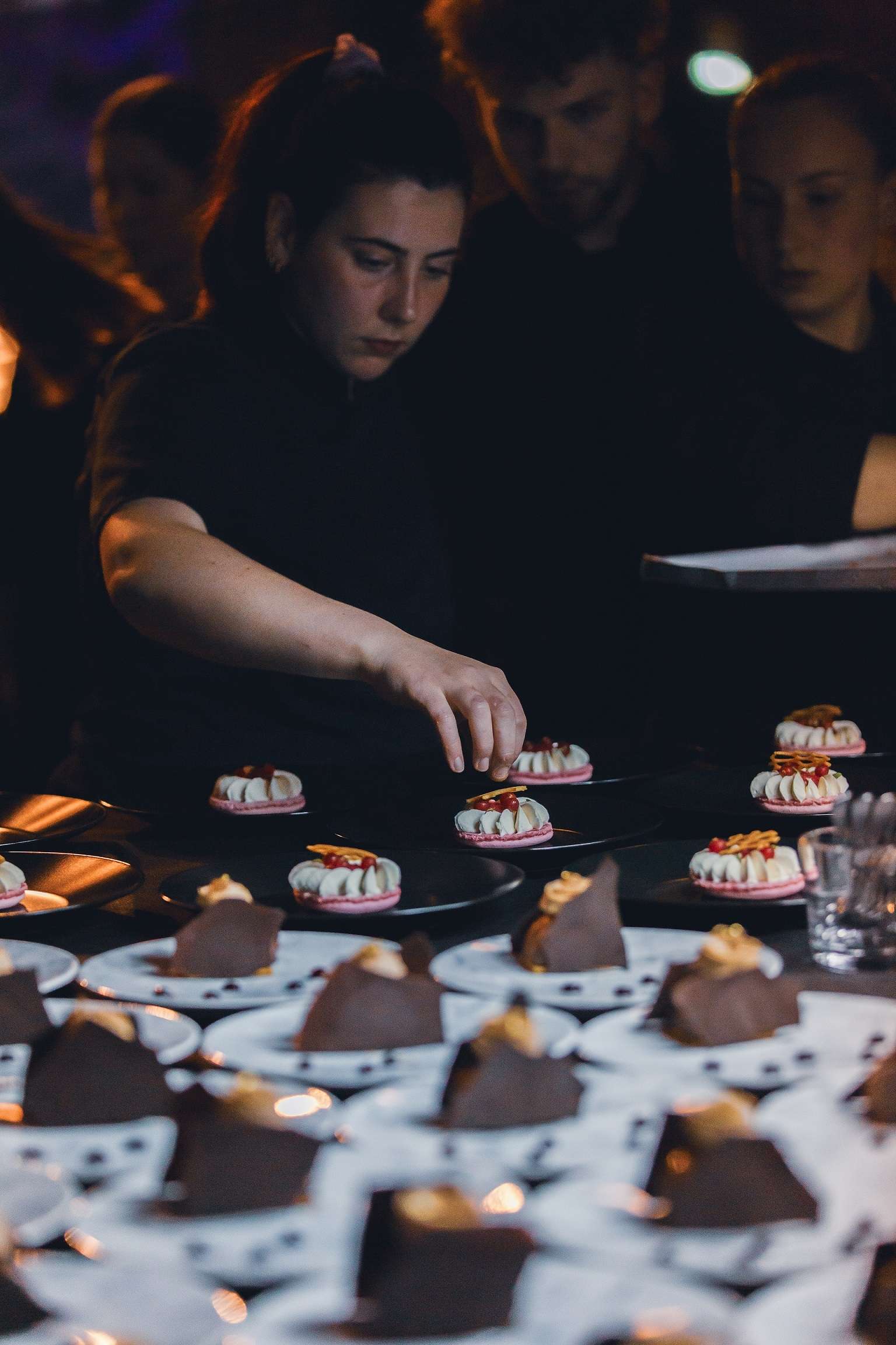 Une jeune femme apporte la touche final à son dessert. Ce dernier est installé parmi une multitude d'autres desserts.