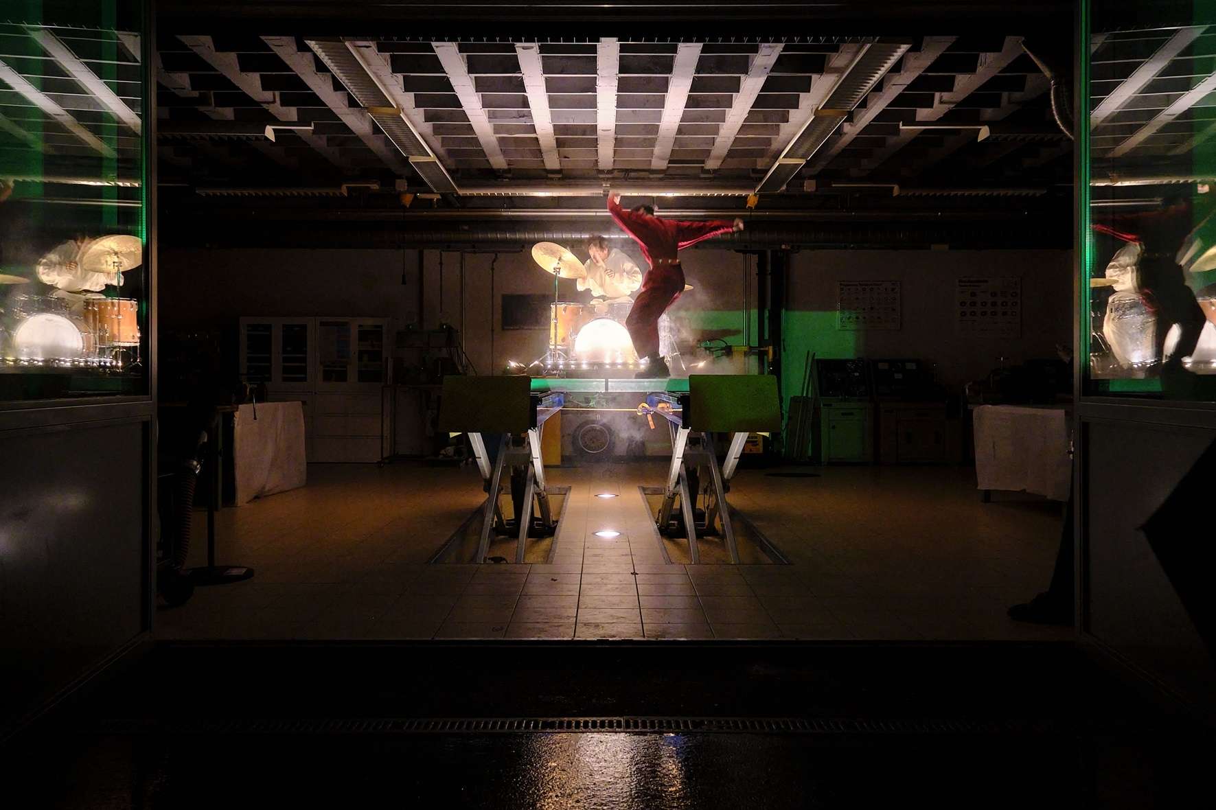 Dans une salle, un musicien joue de la batterie en hauteur sur une table. Une performeuse danse sur la table les bras levés. 