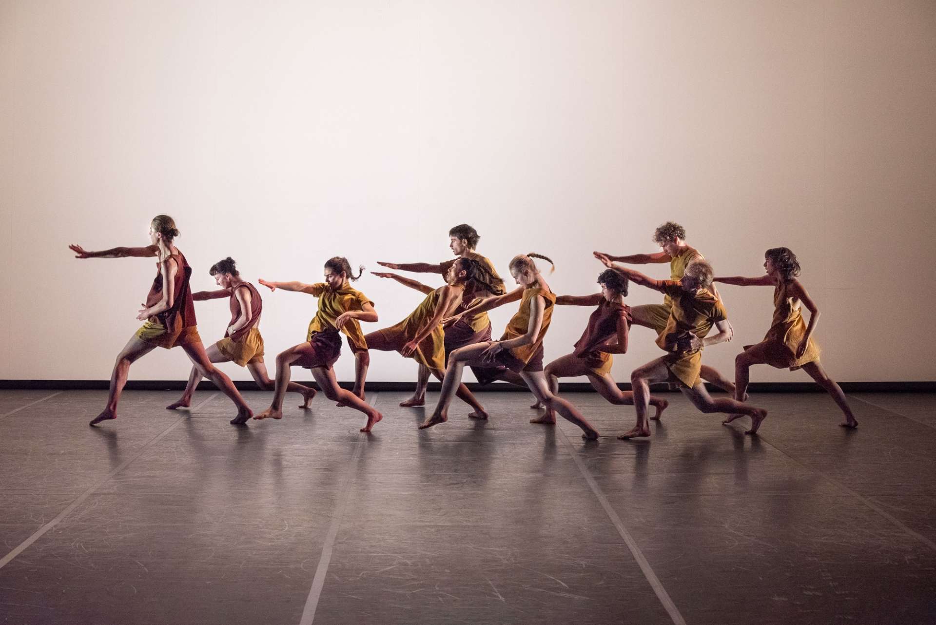 Sur fond blanc, un groupe interprètes de l'ensemble chorégraphique du conservatoire de Paris réalisent un mouvement de ballet. Leurs tenues sont jaune. 