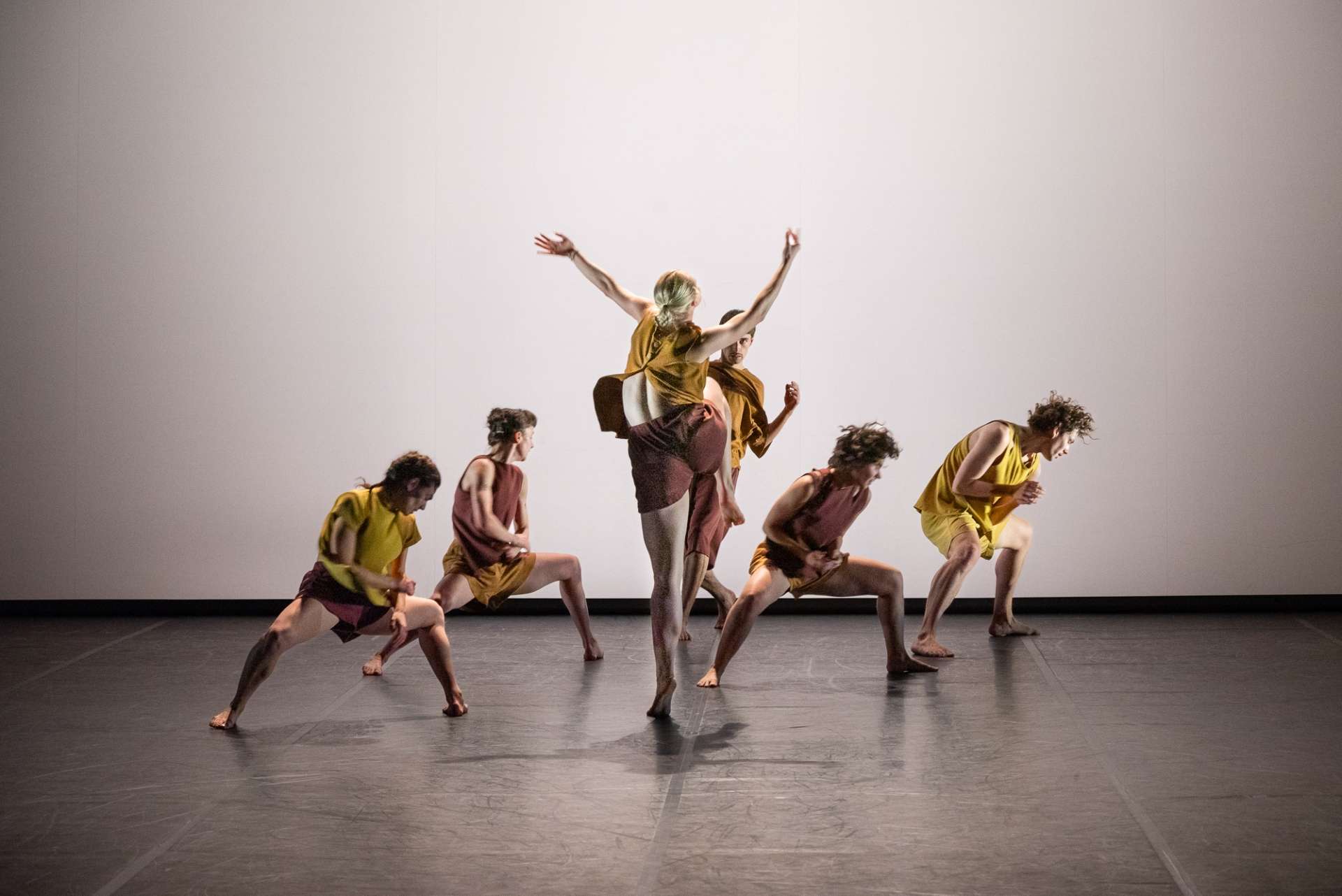 Sur fond blanc, un groupe interprètes de l'ensemble chorégraphique du conservatoire de Paris dansent au centre de la scène. Leurs tenues sont jaune. 