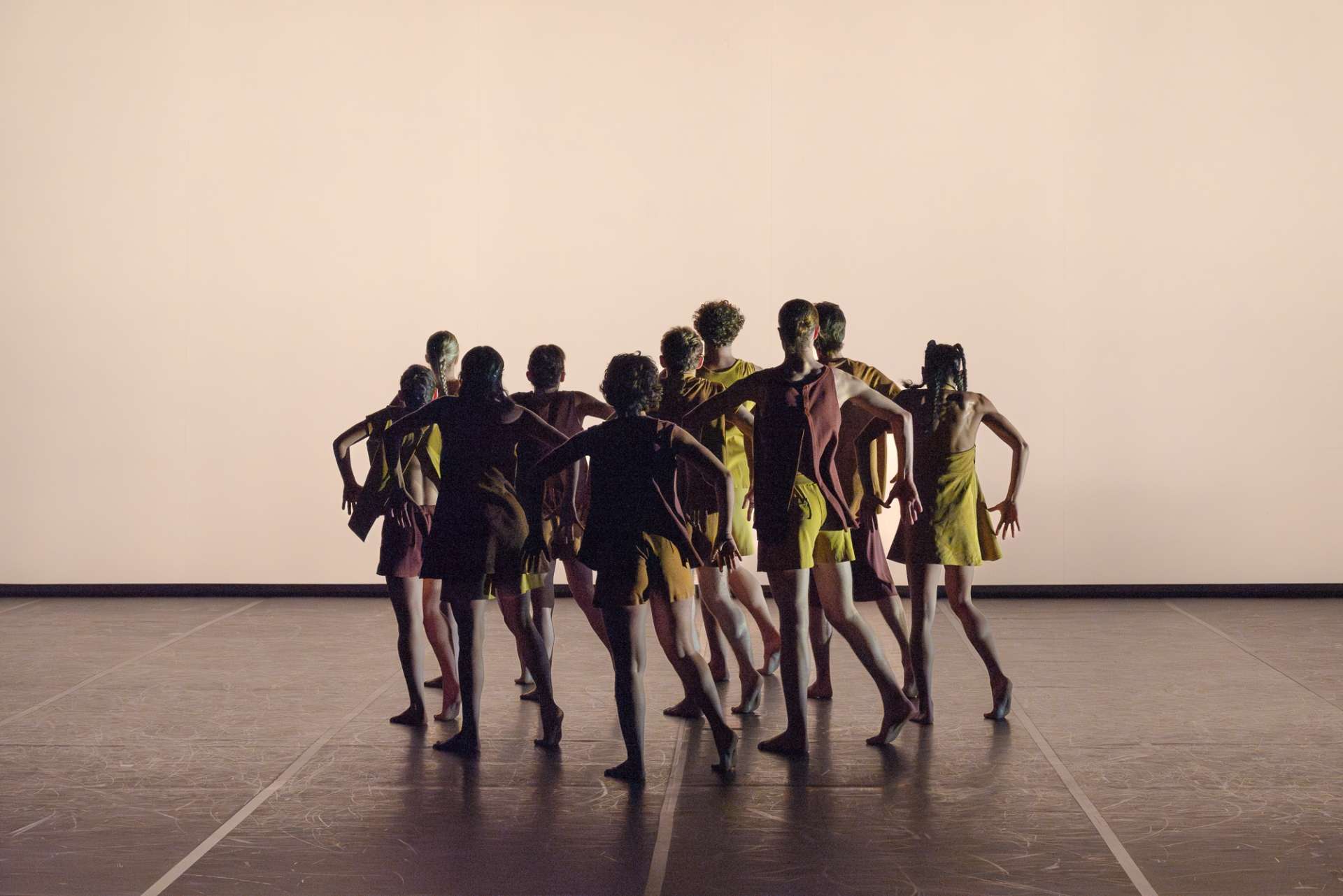 Sur fond blanc, un groupe interprètes de l'ensemble chorégraphique du conservatoire de Paris dansent au centre de la scène. Leurs tenues sont jaune. 
