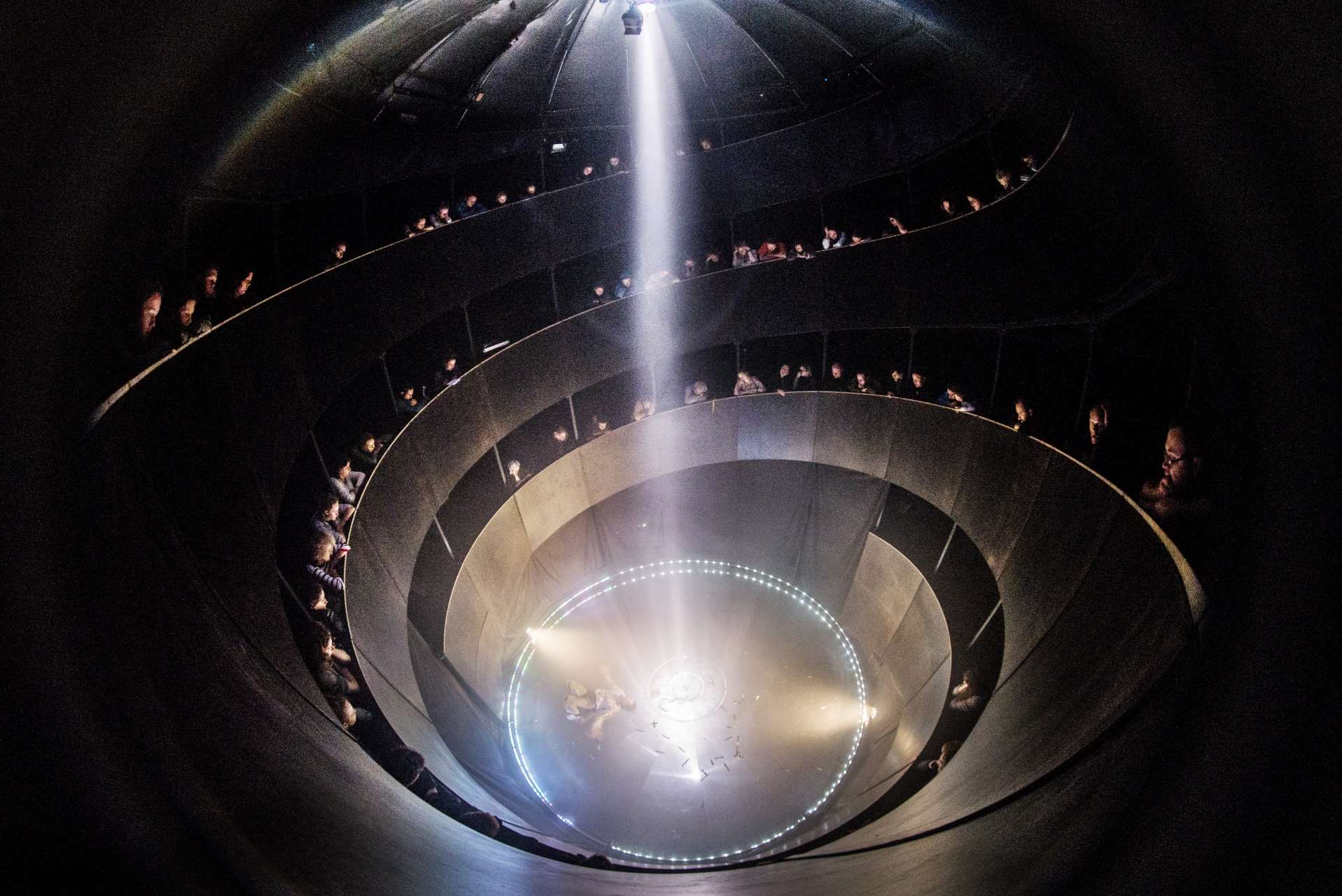 Aperçu du silo pour L'Absolu vu du haut, un rayon de lumière est projeté du haut et les spectateurs et spectatrices sont installé.es tout autour. 
