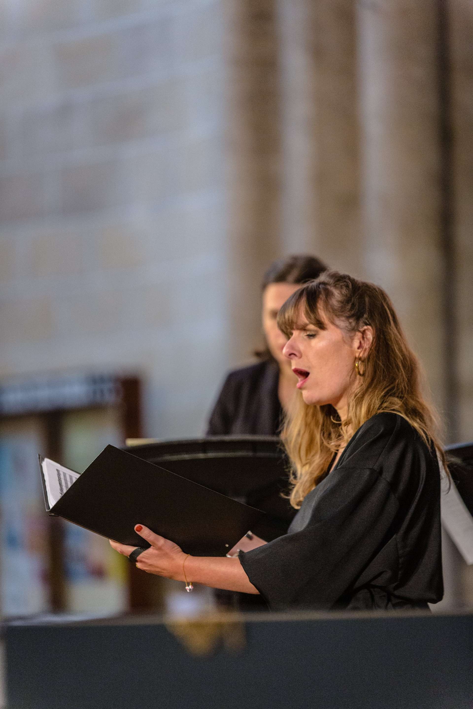 Photo de la représentation de l'ensemble de L'Escadron volant de la reine. Un livre ouvert dans la main, une femme chante. 