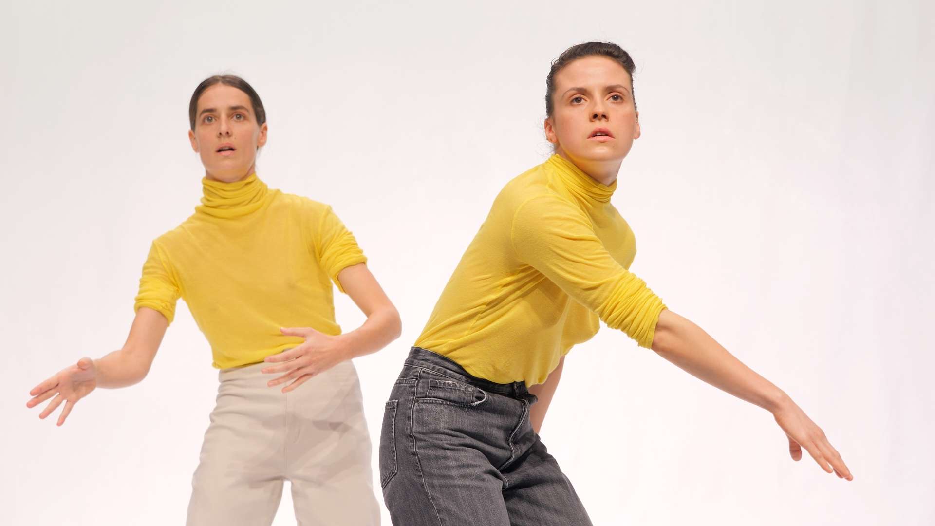 Les deux danseuses du spectacle, arborent le même pull-over à col roulé jaune et se tiennent debout dans une posture chorégraphique.